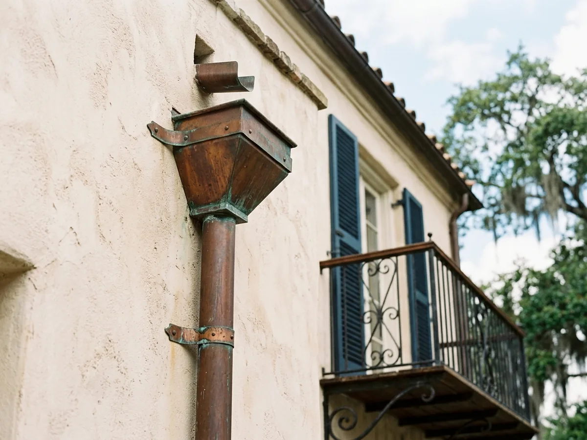 Copper conductor head on a stucco wall feeding a round copper downspout held with copper straps