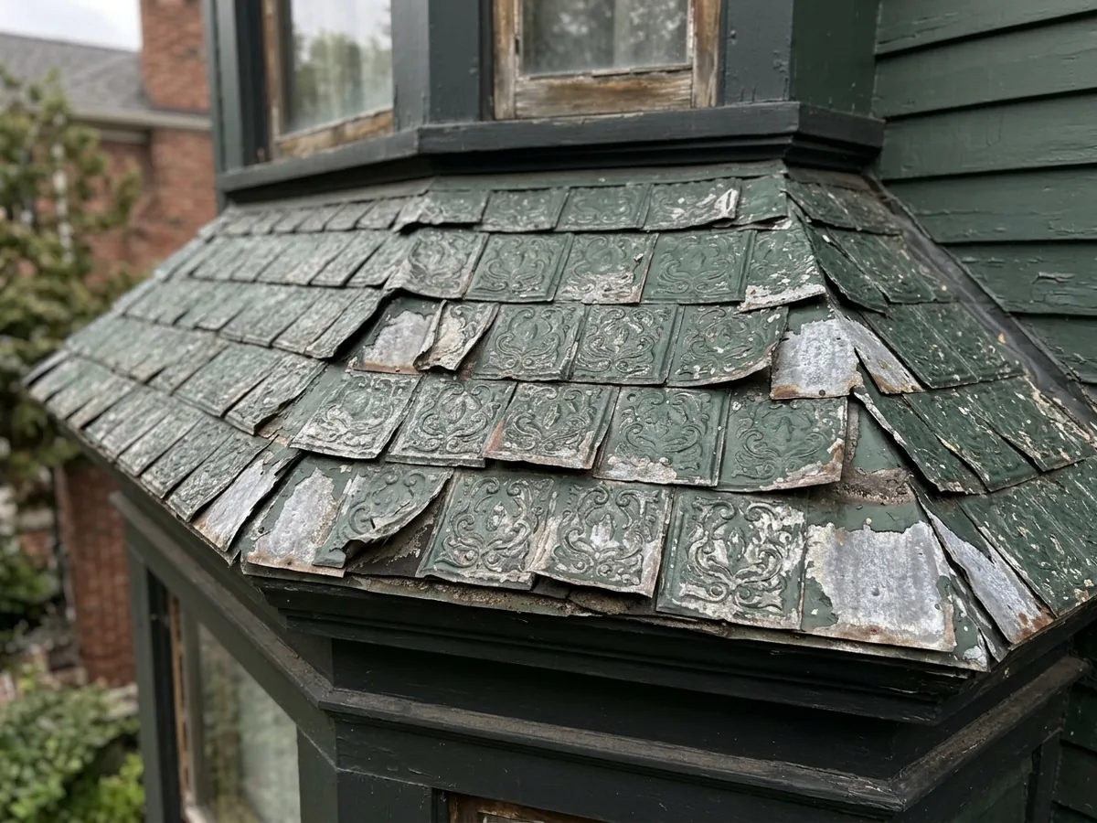 Old roof of small embossed metal shingles with a raised decorative pattern, painted dark green and partly worn