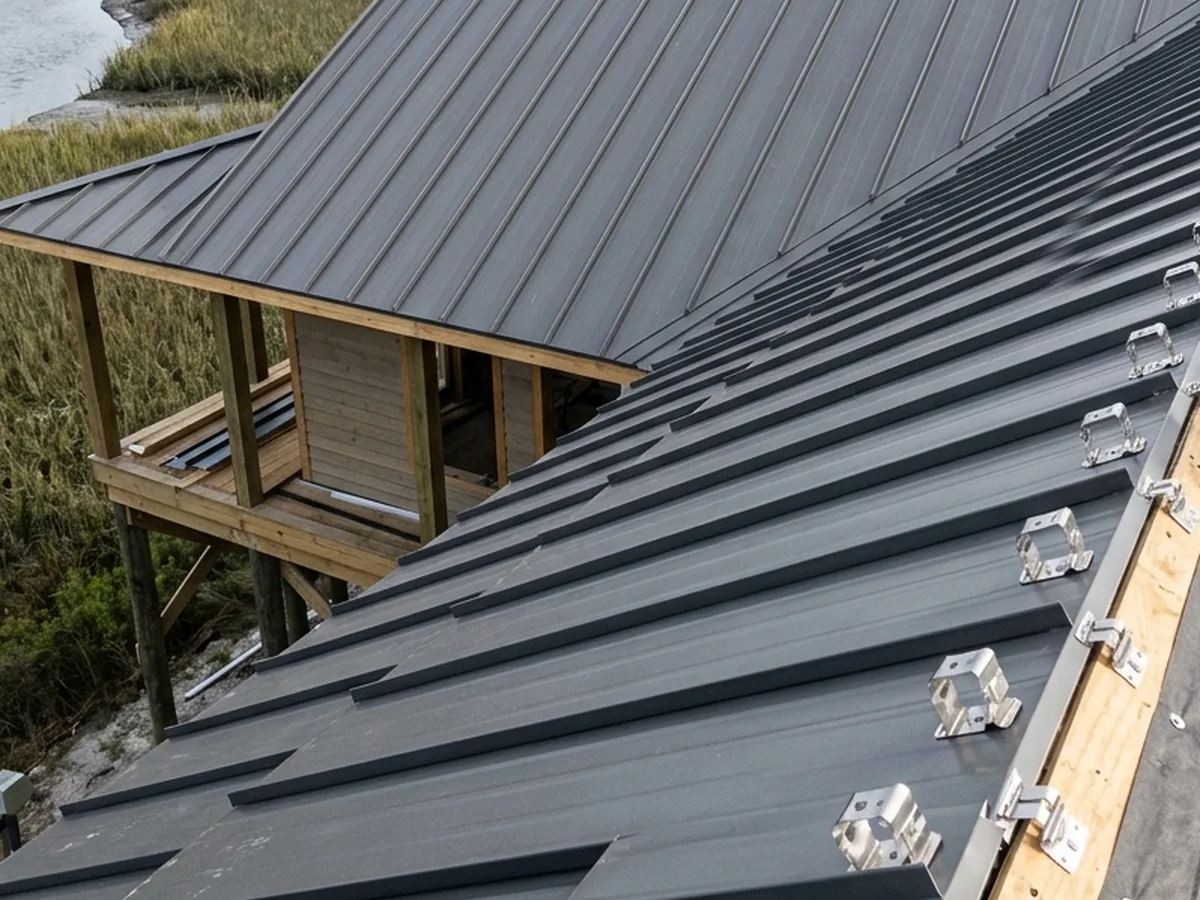 Rows of stainless steel clips and screws along a standing seam roof on a raised house above a marsh