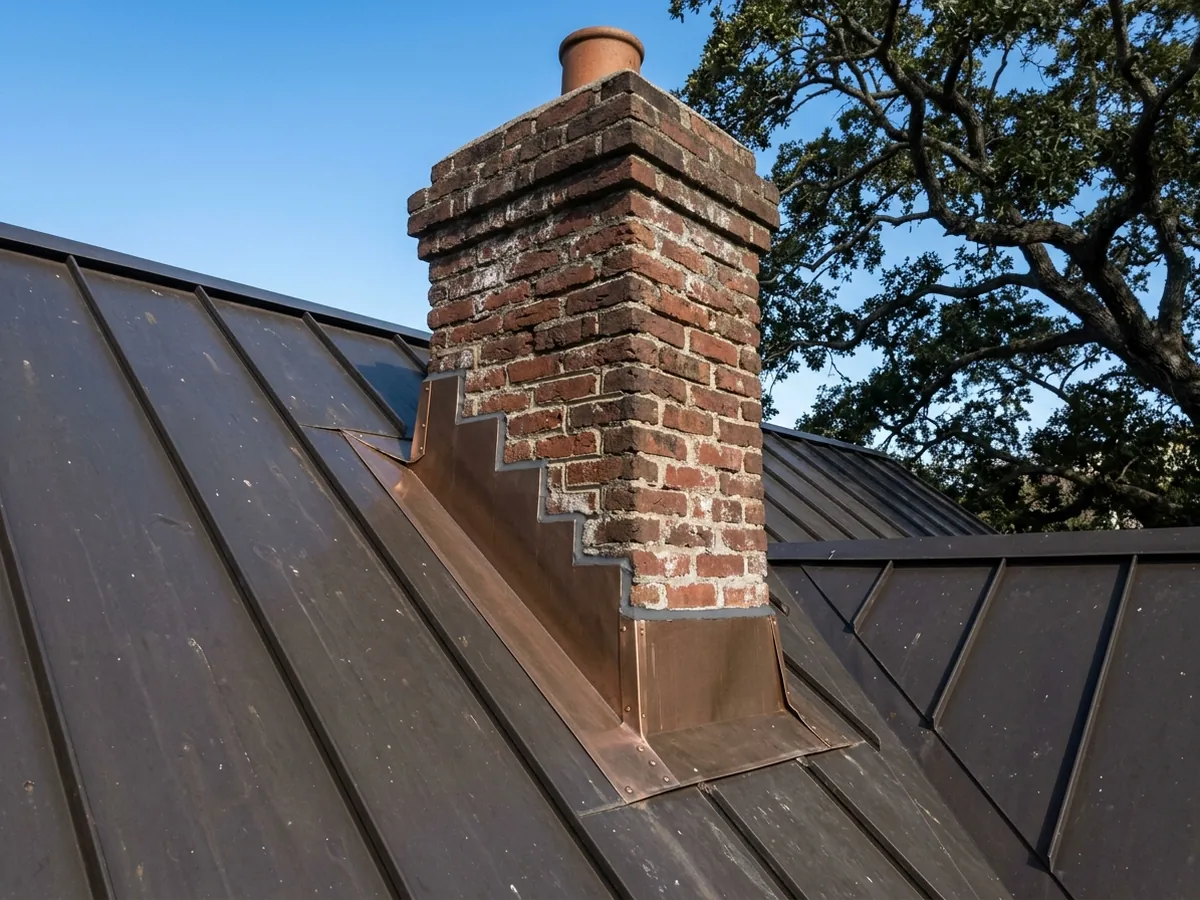 Chimney on a metal roof with new step flashing and counterflashing in matching bronze metal along the brick
