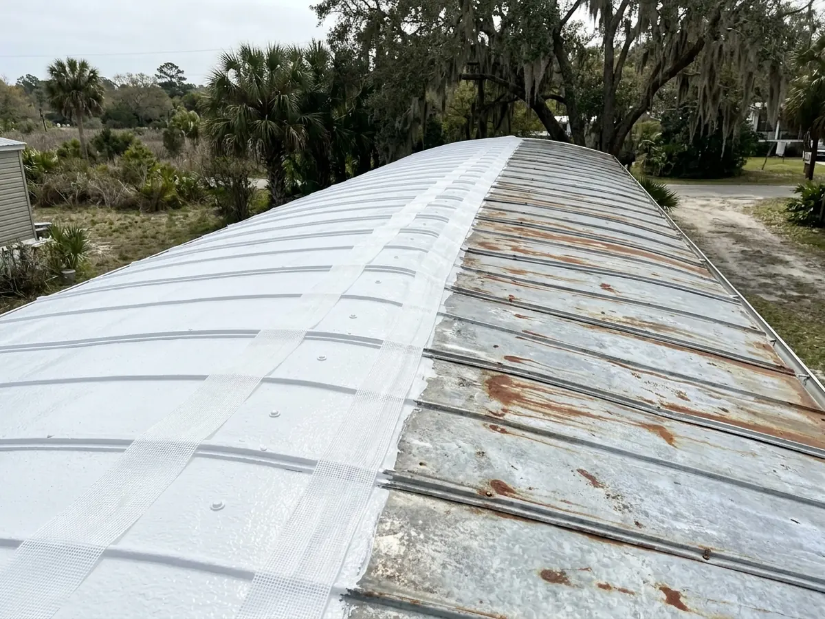 Low curved metal roof of a mobile home with a fresh coat of white elastomeric coating over the seams and fasteners